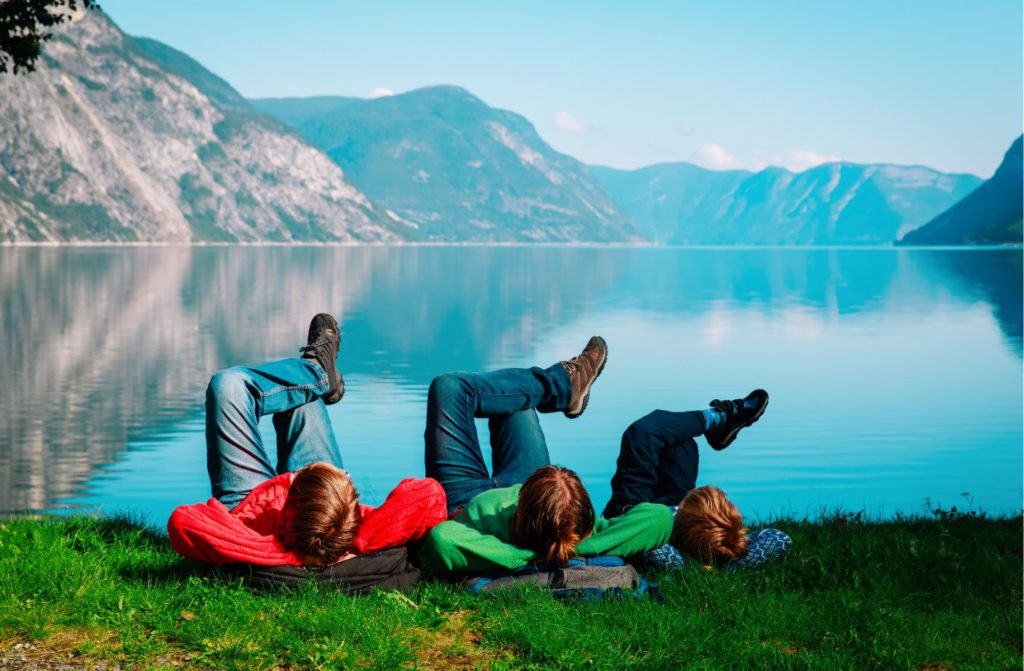 Three boys relaxing next to a lake surrounded by a mountains